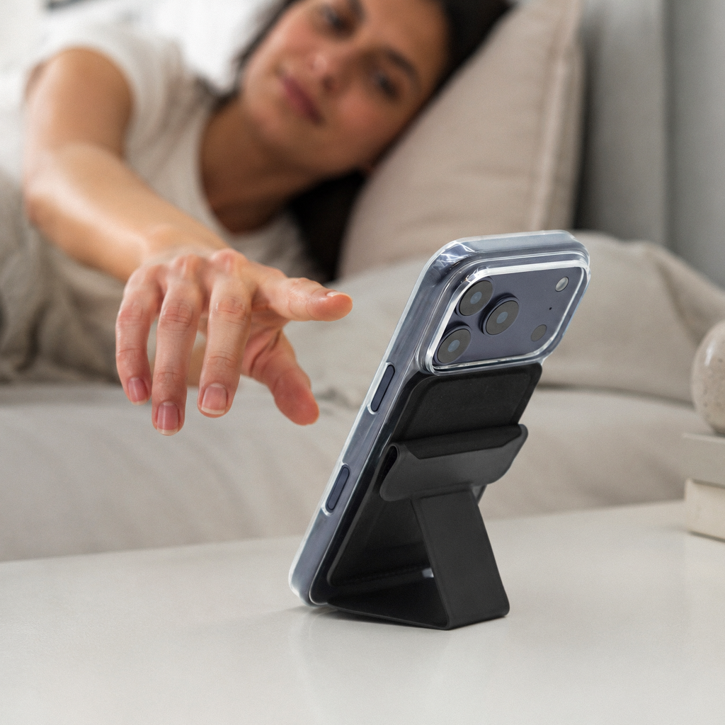 Person reaching for an iPhone held upright by the Peel Magnetic Wallet Stand on a side table